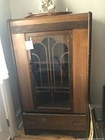 Front view of antique wooden cabinet with glass door and bottom drawer showing waterfall directional pattern on glass.