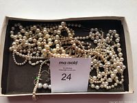 Multiple pearl necklaces tangled inside a black box with varying bead sizes and color tones from white to off-white.