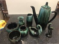 Blue Mountain Pottery ceramic coffee pot, vases, small bowls, swan-shaped bowl, and deer figurine all displayed on dark surface.