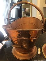 Photo of a large hammered copper bucket with a high curved handle and a sturdy base, polished with minor wear.