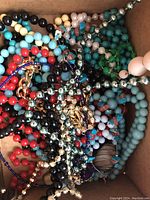 Photo of multiple colorful bead necklaces featuring various bead sizes and colors, including red, turquoise, black, cream, and metallic silver beads tangled together in a box.