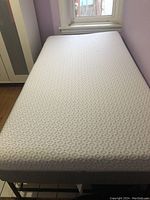 Top-down view of twin mattress on frame showing quilted white cover and grey sides