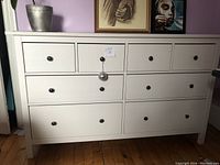 Front view of white dresser showing four small top drawers and four larger lower drawers with black round knobs