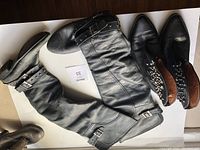 Photo showing three pairs of women's leather boots including tall black boots with buckle straps, short black boots with studs and buckles, and black/brown boots with studs.