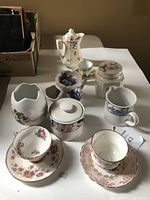 Limoges vase, various tea cups, cream and sugar containers, and decorative porcelain items arranged on white surface.