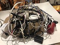 Top view photo of tangled assorted cords and chargers lying on a table, showing cables in black, white, and braided designs.