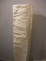 First lamp with tall rectangular white crinkled paper shade against a light wall.