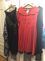 Four plus size dresses hanging on hangers including a bright red double-breasted dress, black satin dress, floral print dress, and a dark colored dress.