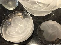 Top view of frosted glass salad bowls and smaller bowls showing embossed swirling leaf pattern on black surface.