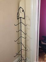 Full view of the wrought iron stand showing vertical pole with six pairs of hooks and the fish head decoration at the top