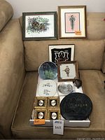 Full view of assorted wall art items arranged on couch, including framed prints and decorative round items laid flat