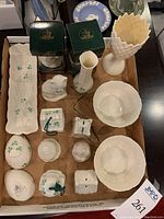 Photo of all Belleek china pieces arranged on a table, including two boxed ornaments, small figurines, bowls, and a long serving dish showing detailed shamrock motifs and fine parian china craftsmanship.