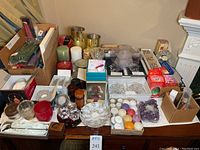 Wide arrangement of assorted candles, glass and metal candle holders, and boxes containing light holders and accessories on a table.