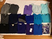 Top view of 17 folded women's cashmere sweaters arranged in rows on a white surface, showcasing variety of colors and styles.
