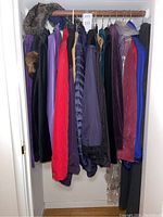 Photo of assorted women's coats hung in a closet, showing a mix of colors and materials including red quilted and purple coats.