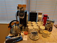 Overview of the coffee and tea items on a kitchen counter showing coffee maker, tea kettle, mugs, capsules holder and other accessories.