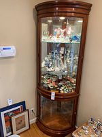 Full view of the corner wooden display cabinet with glass doors showing porcelain and glass figurines inside.