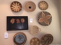 Wall display of six woven baskets and a black Couroc tray with three wood inlaid birds.