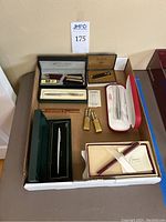 All items overview in a cardboard box showing pens, pencil sets, lighter and accessories.