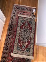 Overview of two stacked fringed oriental-style rugs, small rug on top of runner on hardwood floor