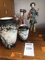 Photo showing two Japanese pottery vases and two colorful porcelain figurines on wood shelf.