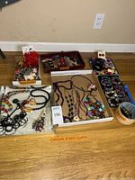 Overview photo of costume jewelry including necklaces, bracelets, and hair clips arranged on floor and trays.