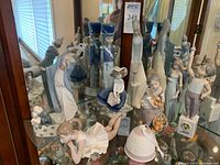 Nine figurines and one bell displayed on glass shelf