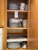 Photo of china and serveware stacked inside a cabinet, showing plates, bowls, cups, and casserole pot all with floral pattern.
