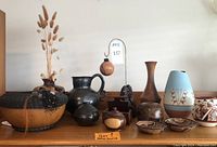 Overall view of back and front rows showing gourd vessel, black pottery, wooden stand, burl and smooth vases, and painted pottery