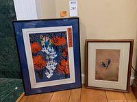 Two framed artworks side by side: a larger Japanese print of people herding geese in a dark frame with blue mat, and a smaller photograph of two bee-eaters by Mangelsen
