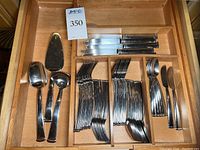 Full drawer view showing flatware assortment arranged including forks, knives, spoons, and serving pieces.