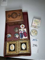 Photo of entire lot showing double layer wood box, porcelain Peter Rabbit box, enamel artframes, worry dolls, glass marbles, metal container, and round spinning box with earrings.