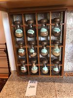Full view of wooden spice rack on countertop holding 12 labeled glass jars with wooden tops.