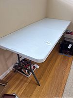 Full view of one white folding table set up with legs extended, showing white surface and gray metal legs