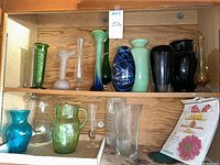 Wooden shelf holding various colored glass vases and pitchers in blue, green, clear and dark hues