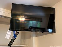 Front view of the 32-inch Samsung flat screen TV mounted on wall with remote control hanging on a shelf below it.