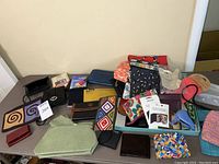Wide view of all wallets, purses, pouches and travel accessories on table.