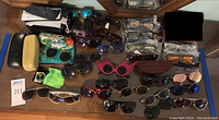 Full overview of sunglasses and reading glasses with cases on wooden floor including boxed and unboxed items