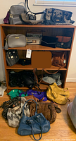 Overview of assorted purses on wood shelving and floor, showing variety of styles, colors and materials