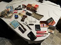 Overview of assorted vintage items arranged on a table, including 35mm camera, grooming products, scissors, reading glasses, and various small cases and boxes.