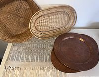 Photo showing two woven baskets, teak tray with copper plate, and part of flat woven rug underneath.