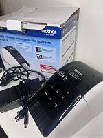 Photo showing Brother QL-810W wireless label printer with power cords and original product box in the background.