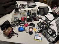 Overview of multiple film, instant and digital cameras, boxes, bags and accessories on a table