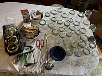 Full display of canning jars, lids, rings, and tools set on a white cloth surface.