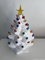 Front and angled view of the white ceramic Christmas tree decorated with multicolored bulb-shaped ornaments and a yellow translucent star topper.