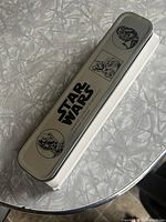 Metal rectangular Star Wars collectible watch case with character illustrations and Star Wars logo on the lid, resting on a silver textured surface.