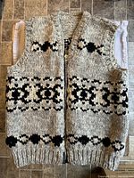 Full front view of the wool vest showing the black geometric pattern on a natural colored background, zipper front, and ribbed hem and armholes.