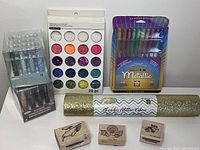 Photo of entire lot showing glitter palette, gel pens, glass beads, glitter fabric roll and wooden stamps
