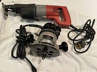 Photo showing the Craftsman red and black reciprocating saw and the Porter-Cable router with attached cords.