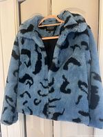 Front view of blue plush coat with black leopard-like patterns hanging on hanger